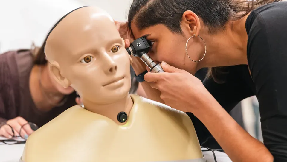 A nursing student practices using an otoscope on a patient simulator